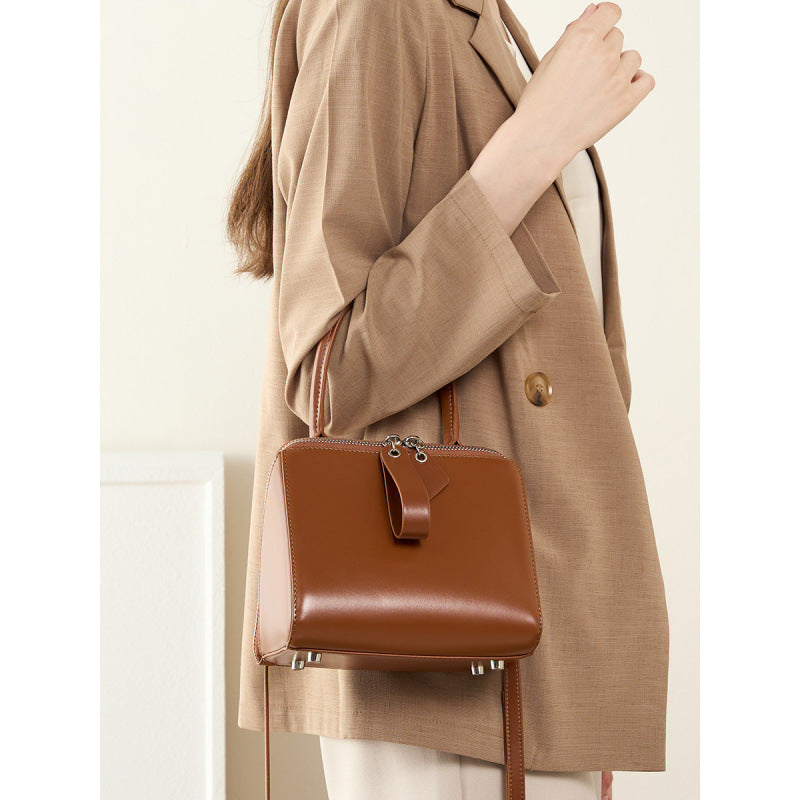 Brown leather handbag held by a person wearing a beige coat.