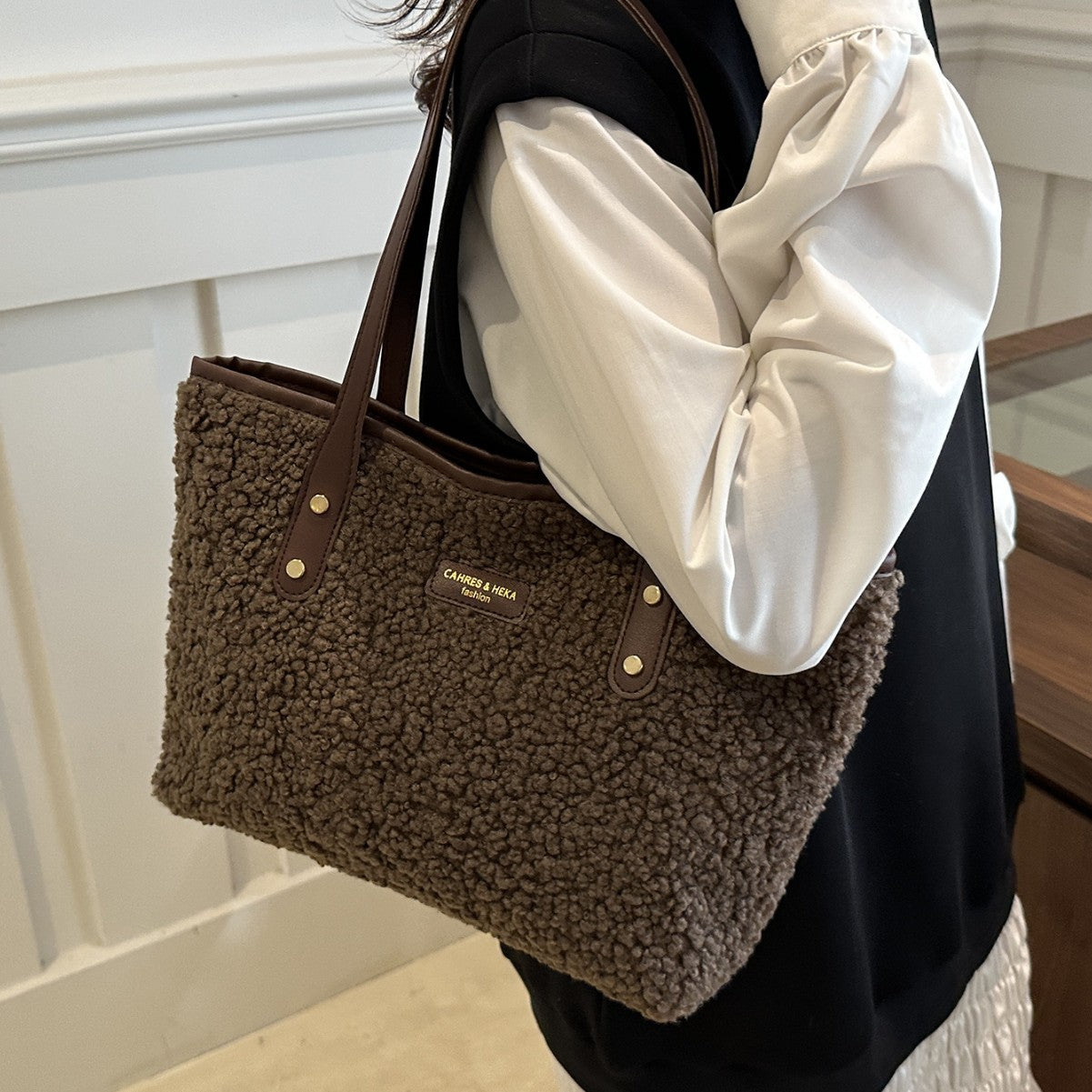 Brown textured handbag with visible brand logo held by a person wearing a white shirt.
