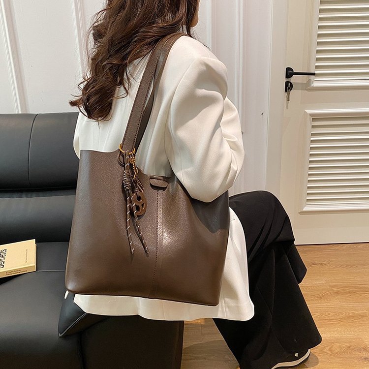 Person holding a brown leather handbag in a room with a couch and door.